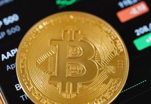 Gold Bitcoin Coin Lying on a Phone Displaying Cryptocurrency Graphs