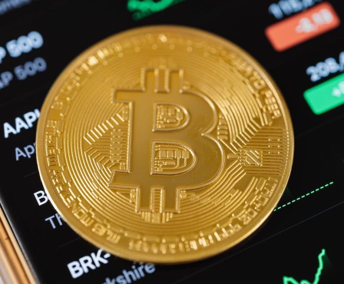 Gold Bitcoin Coin Lying on a Phone Displaying Cryptocurrency Graphs