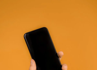 A hand holding a black cell phone Description automatically generated